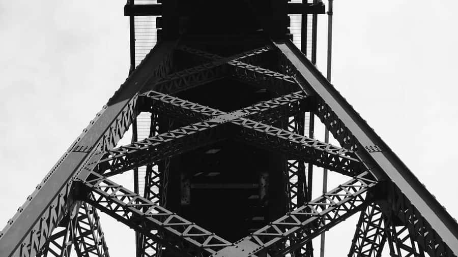 This black and white image shows the intricate steel framework of a tall tower, creating a visually striking geometric pattern.