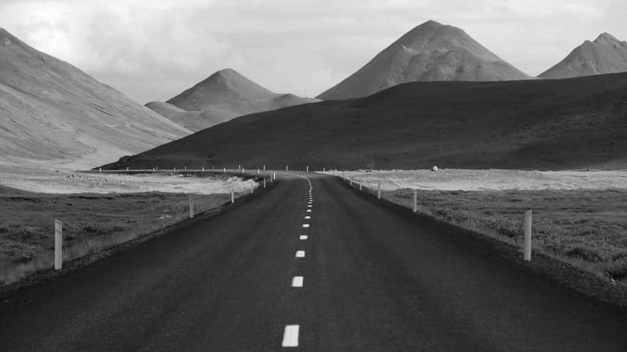 This image shows a long, winding road leading through a desolate, mountainous landscape in black and white.